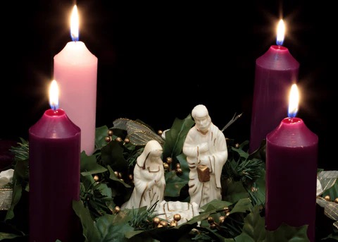 Advent wreath with four lit candles surrounding a nativity scene
