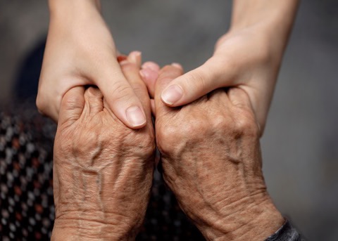 Younger hands gently holding the hands of an elderly person
