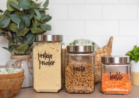 on the kitchen counter, labeled jars of protein powder, pasta, and lentils
