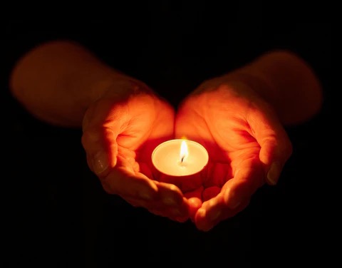 holding a small tea light candle in cupped hands in the darkness