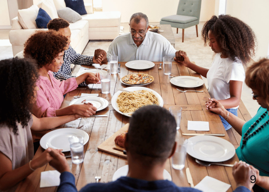 a family saying prayers before their meal, they are all seated at the table