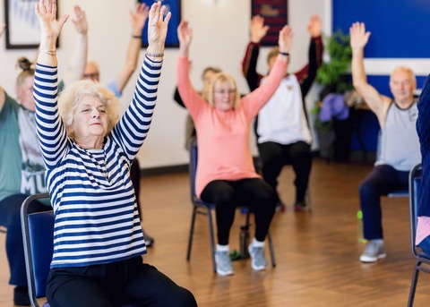 elderly women stretching while sitting in chairs