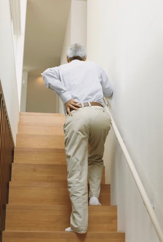 elderly man climbing stairs with his hand on his back
