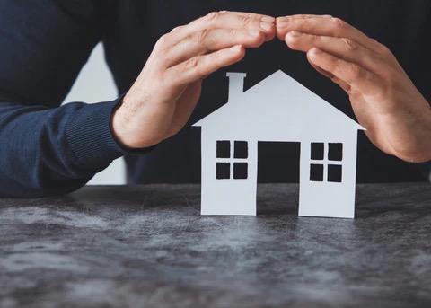 a cut out of a house with a man holding his hands over it as if to protect it