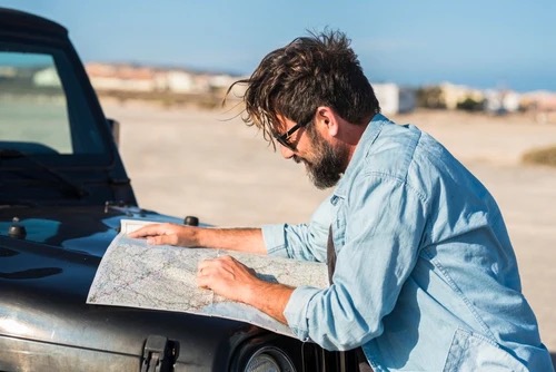  a man standing outside his vehicle looking at a paper map