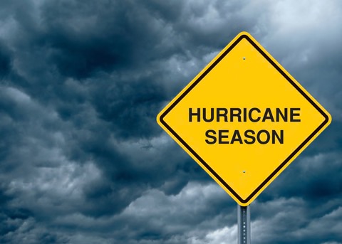 storm clouds in the background with a bright yellow sign that reads with black letters "Hurricane Season"
