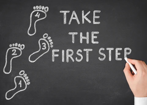 a chalkboard with white footprints with the words "Take The First Step"