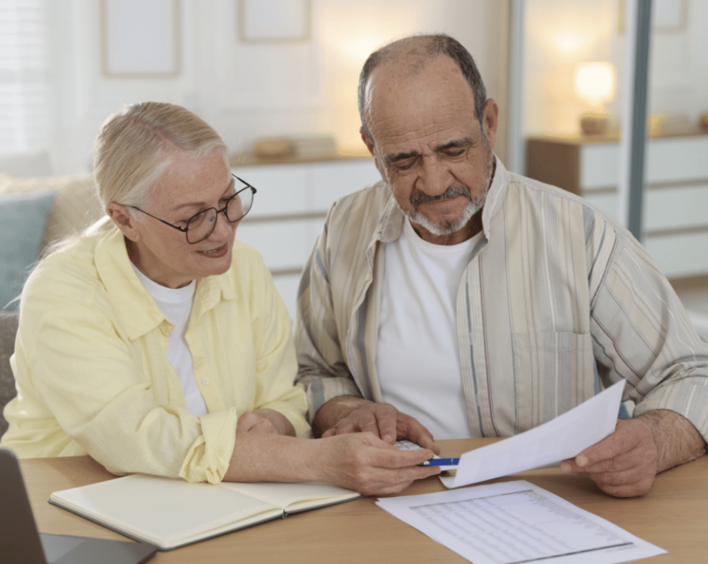 couple planning their three month strategy - an older couple sitting at a table with a notebook and looking at papers.